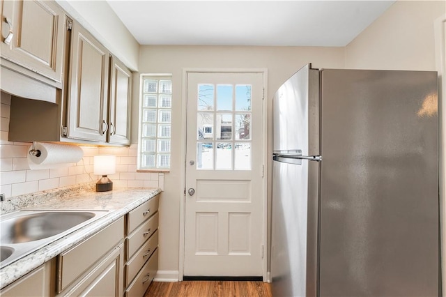 kitchen with sink, decorative backsplash, light wood-type flooring, light stone countertops, and stainless steel refrigerator