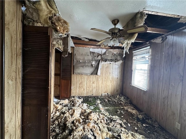 misc room with wood walls, ceiling fan, and a textured ceiling