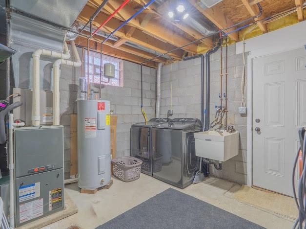 basement featuring electric water heater, washing machine and dryer, and sink