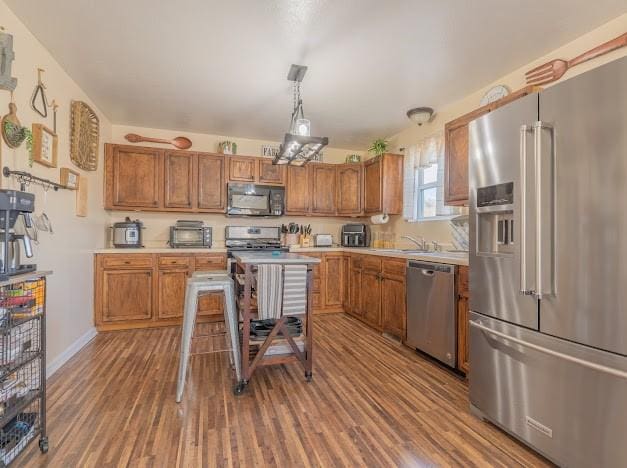 kitchen featuring sink, stainless steel appliances, decorative light fixtures, a kitchen bar, and hardwood / wood-style flooring