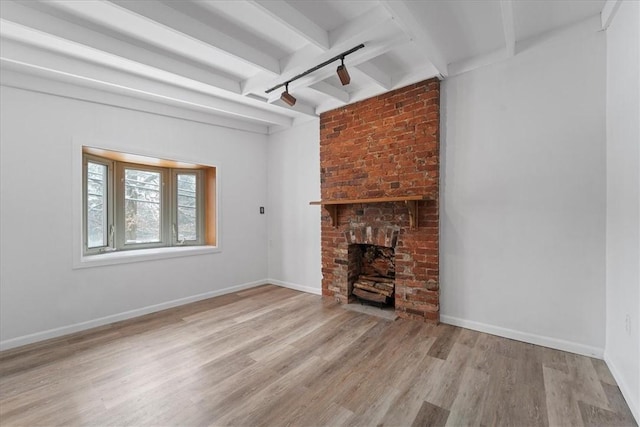 unfurnished living room with a fireplace, beam ceiling, rail lighting, and light hardwood / wood-style flooring