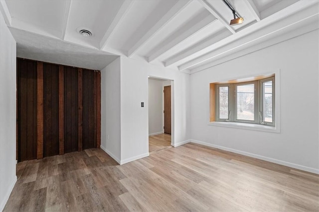 spare room featuring beamed ceiling and light wood-type flooring