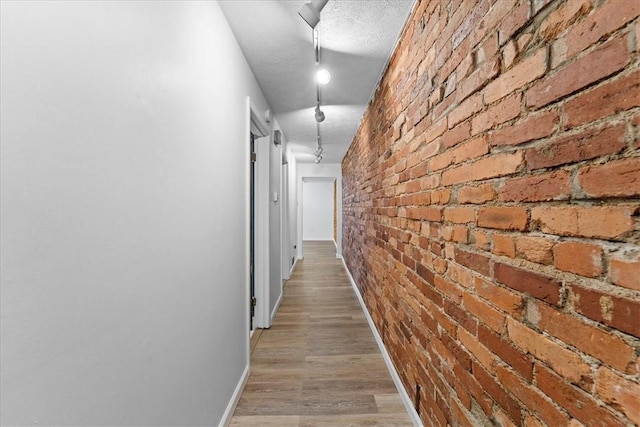 corridor featuring a textured ceiling, brick wall, and light hardwood / wood-style flooring