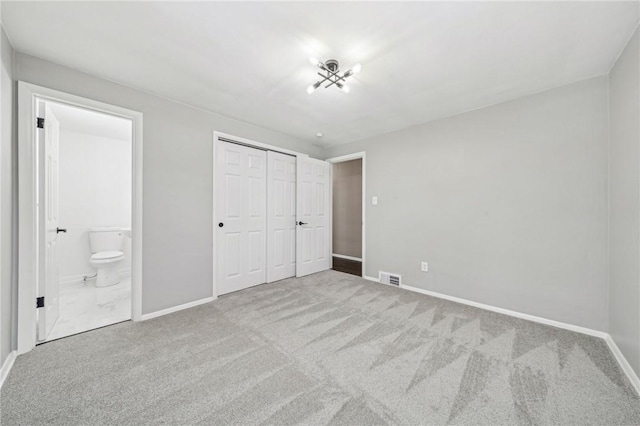 unfurnished bedroom featuring ensuite bath, light carpet, and a closet