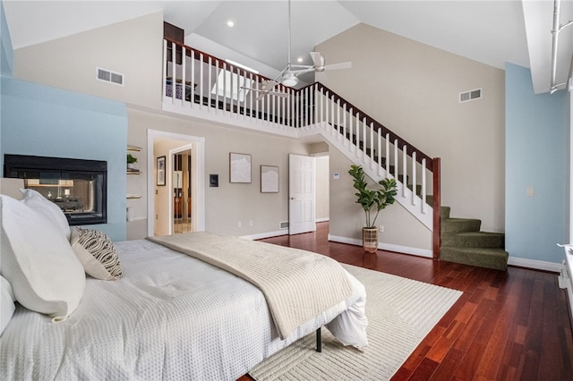 bedroom with a multi sided fireplace, dark hardwood / wood-style floors, and high vaulted ceiling