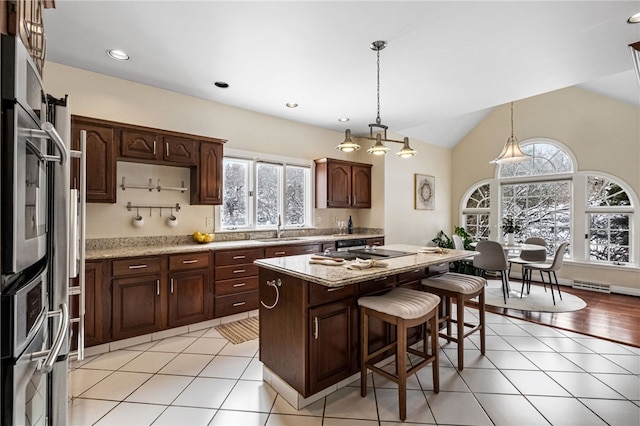 kitchen featuring dark brown cabinetry, a center island, hanging light fixtures, and sink