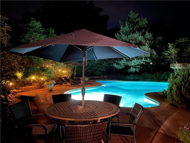 pool at night featuring a patio area