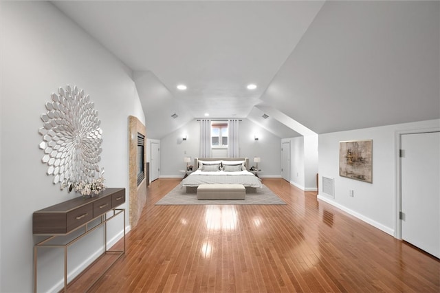 unfurnished bedroom with a fireplace, light hardwood / wood-style flooring, and vaulted ceiling