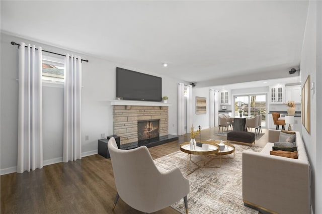 living room with a stone fireplace and dark wood-type flooring