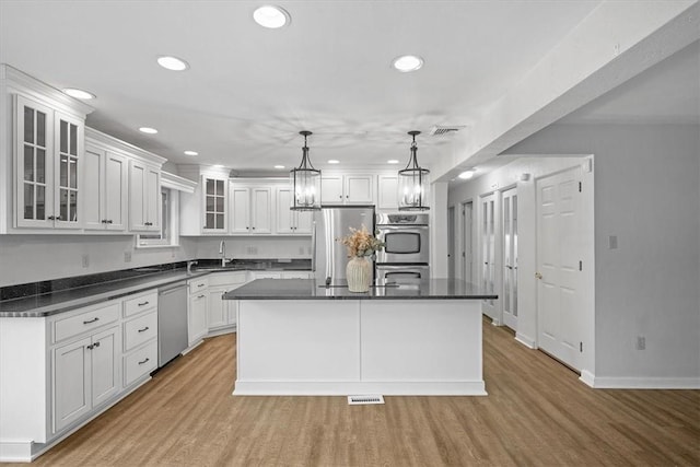 kitchen featuring a center island, stainless steel appliances, hanging light fixtures, light hardwood / wood-style flooring, and white cabinets