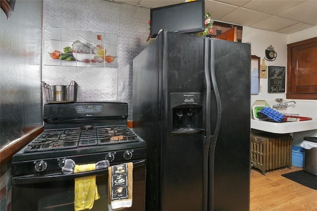 kitchen with a paneled ceiling, light hardwood / wood-style floors, and black appliances