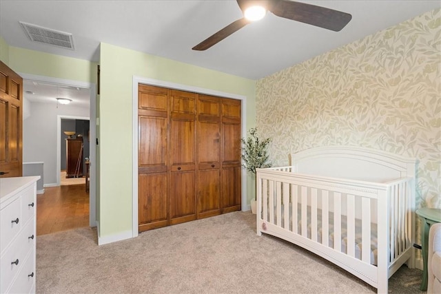 bedroom featuring ceiling fan, a closet, a nursery area, and light carpet