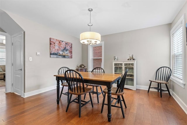 dining area with wood-type flooring, a wealth of natural light, and a notable chandelier