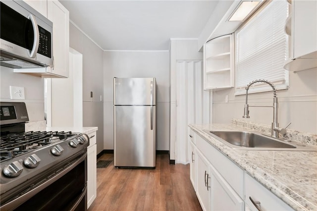 kitchen with sink, light stone counters, appliances with stainless steel finishes, white cabinets, and hardwood / wood-style flooring