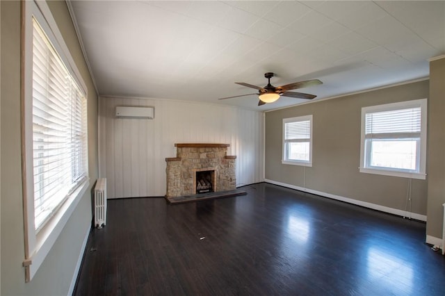 unfurnished living room with radiator heating unit, a wall unit AC, a stone fireplace, and a healthy amount of sunlight