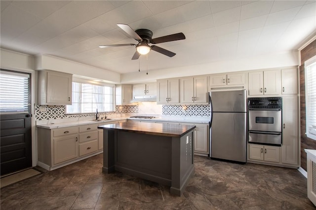 kitchen with ceiling fan, sink, a center island, stainless steel appliances, and backsplash