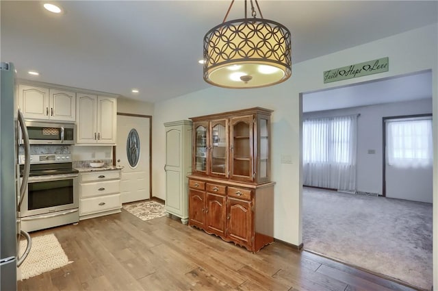 kitchen featuring white cabinetry, hanging light fixtures, stainless steel appliances, and light hardwood / wood-style floors