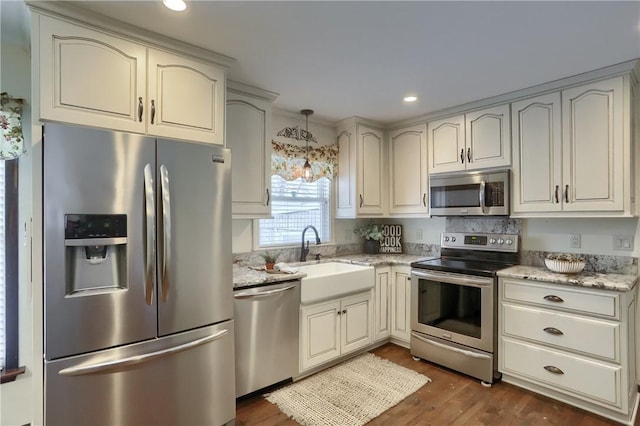 kitchen with light stone countertops, stainless steel appliances, sink, pendant lighting, and dark hardwood / wood-style floors