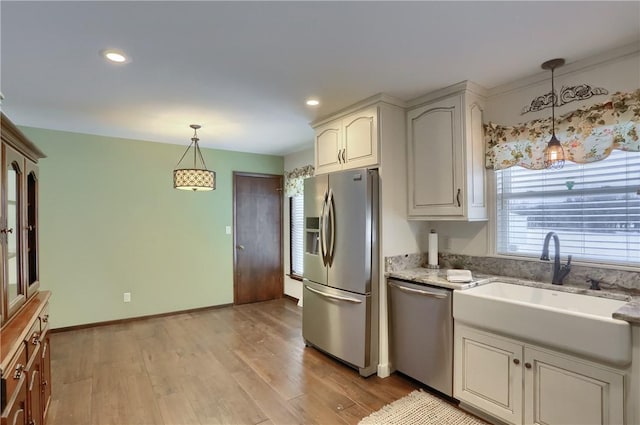 kitchen featuring light stone countertops, appliances with stainless steel finishes, light wood-type flooring, sink, and decorative light fixtures