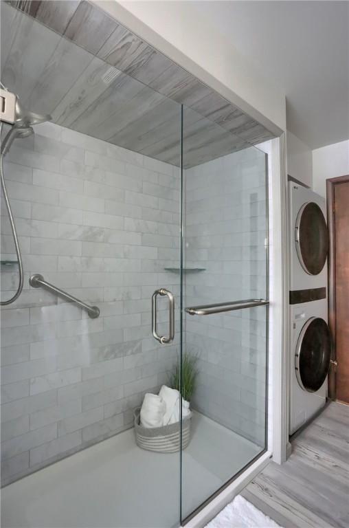 bathroom featuring a shower with door and stacked washer and clothes dryer