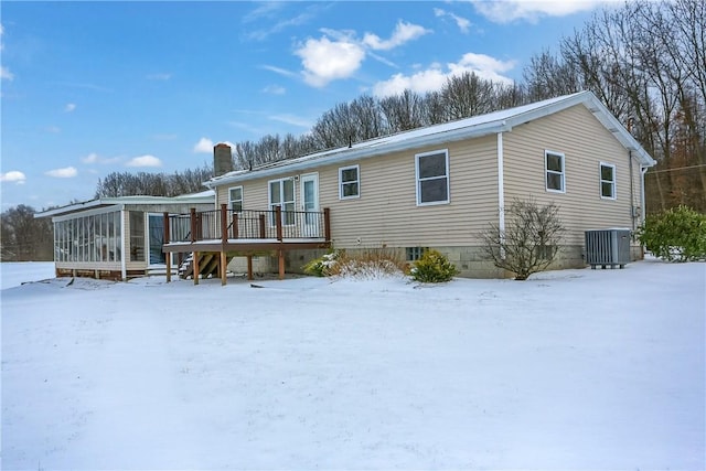 snow covered house with central AC unit, a sunroom, and a deck