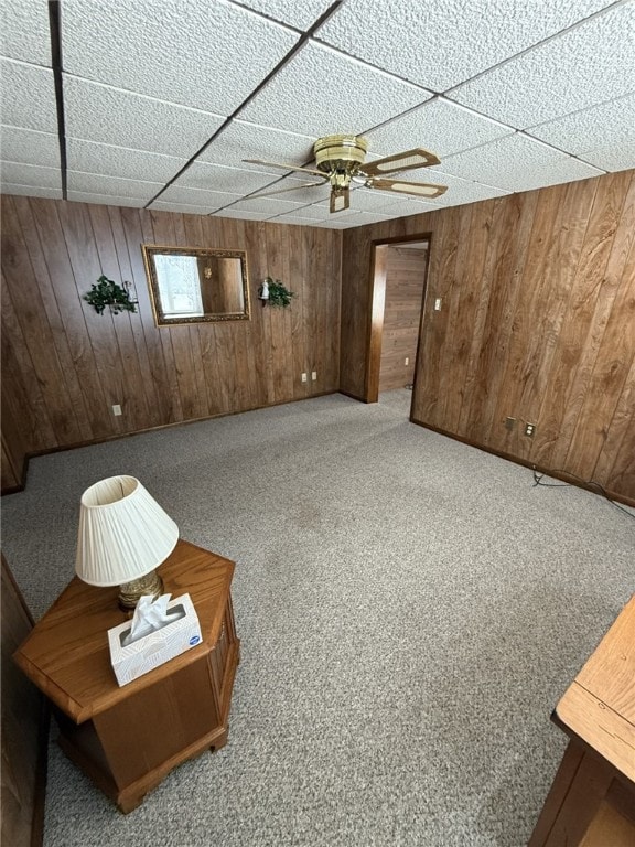 interior space with carpet flooring, wood walls, a drop ceiling, and ceiling fan