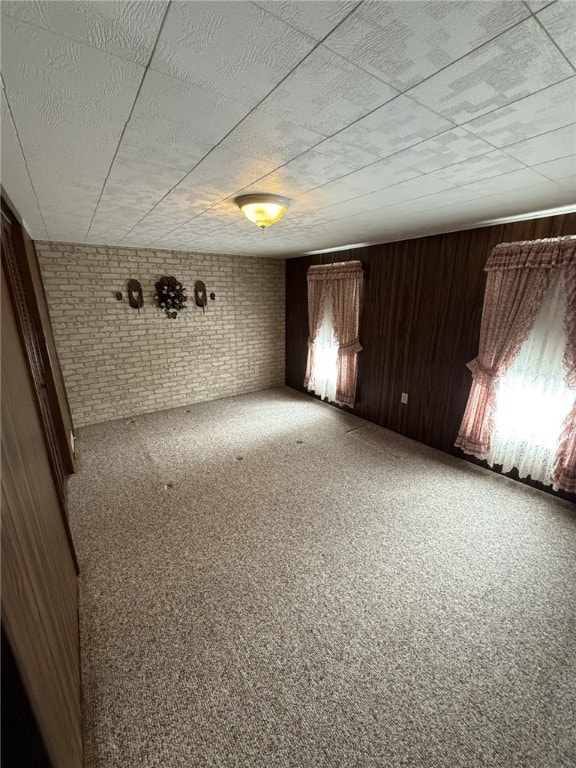 unfurnished room featuring carpet flooring, wood walls, and brick wall