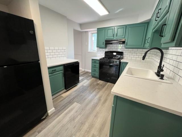 kitchen with black appliances, green cabinets, sink, and light hardwood / wood-style flooring