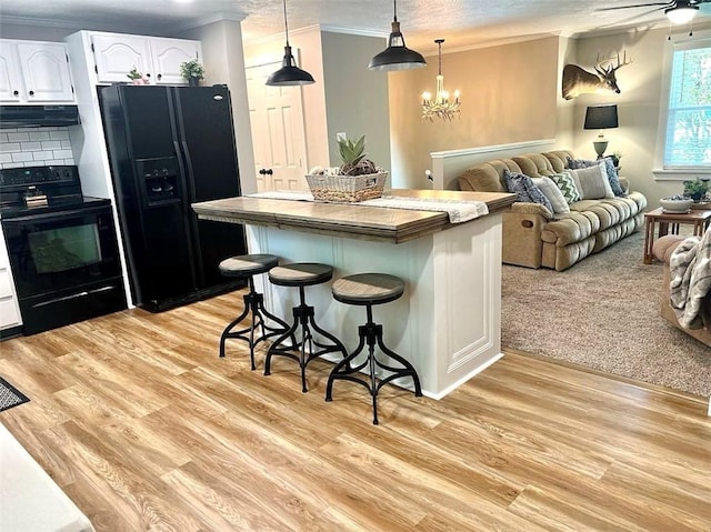 kitchen featuring a kitchen breakfast bar, exhaust hood, black appliances, a center island, and white cabinetry