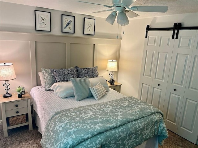 bedroom featuring a barn door, ceiling fan, and dark carpet