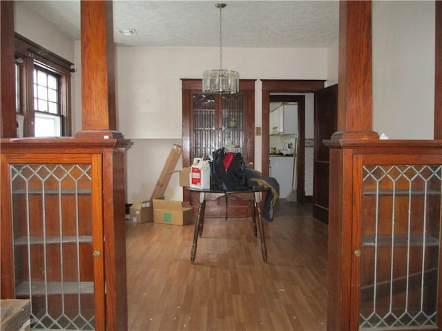 dining area featuring wood-type flooring, a textured ceiling, an inviting chandelier, and ornate columns