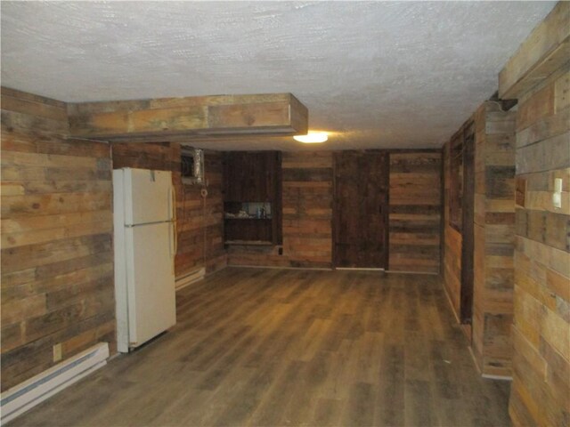 basement with a textured ceiling, dark wood-type flooring, white refrigerator, a baseboard radiator, and wood walls