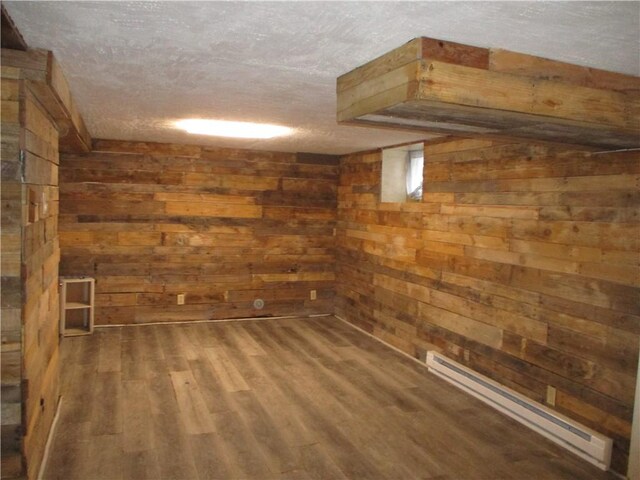 basement with wooden walls, wood-type flooring, a textured ceiling, and a baseboard heating unit