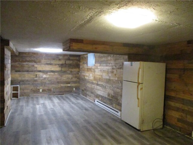 basement featuring baseboard heating, white refrigerator, wood walls, wood-type flooring, and a textured ceiling