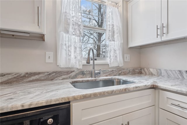 kitchen with dishwasher, light stone counters, white cabinetry, and sink