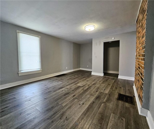 unfurnished room featuring dark wood-type flooring, visible vents, and baseboards