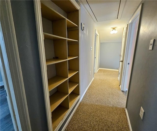 hall featuring attic access, carpet flooring, and baseboards