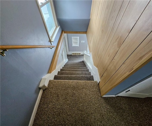 stairway with visible vents, a textured wall, wooden walls, and baseboards