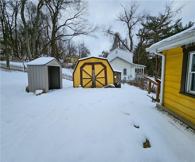 yard layered in snow featuring a shed, fence, and an outbuilding