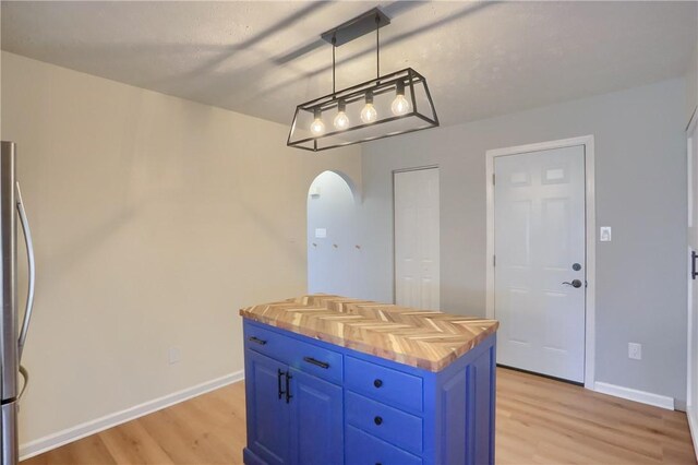 kitchen featuring pendant lighting, a center island, blue cabinets, stainless steel fridge, and butcher block countertops