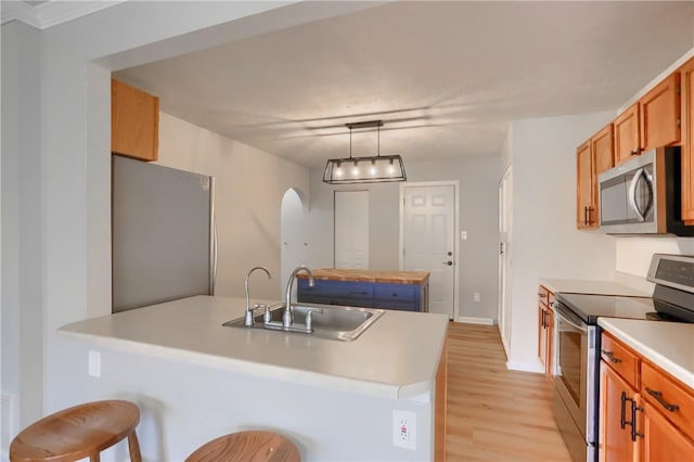 kitchen featuring a kitchen bar, stainless steel appliances, sink, decorative light fixtures, and light hardwood / wood-style flooring