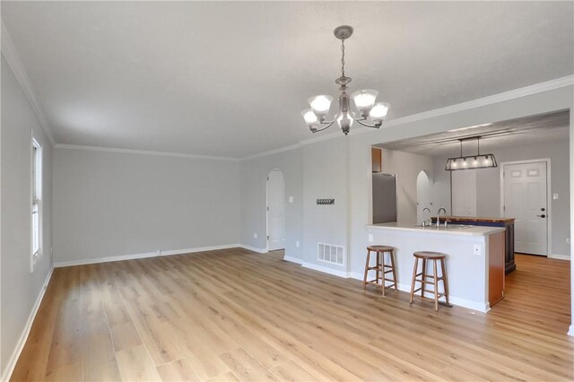 kitchen featuring a breakfast bar, sink, hanging light fixtures, ornamental molding, and stainless steel refrigerator