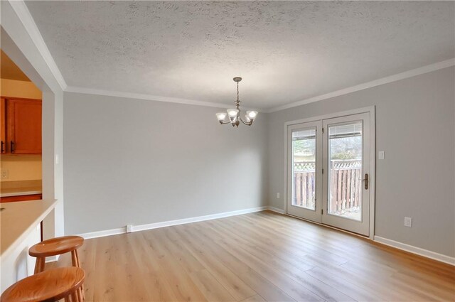 unfurnished dining area with light wood-type flooring, a textured ceiling, crown molding, and a notable chandelier