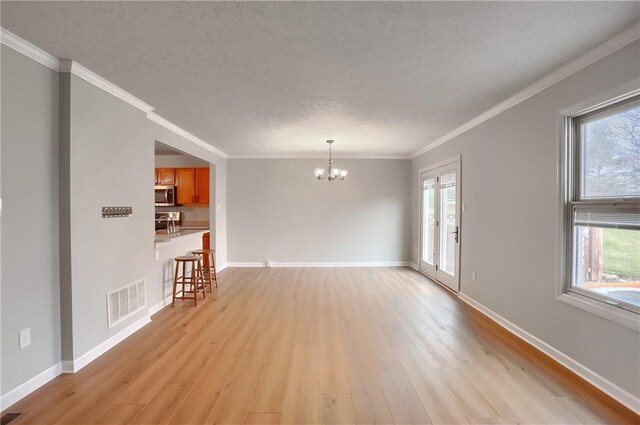 spare room with a textured ceiling, light wood-type flooring, crown molding, and an inviting chandelier