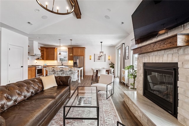 living room with dark wood-type flooring, sink, a chandelier, vaulted ceiling with beams, and a stone fireplace