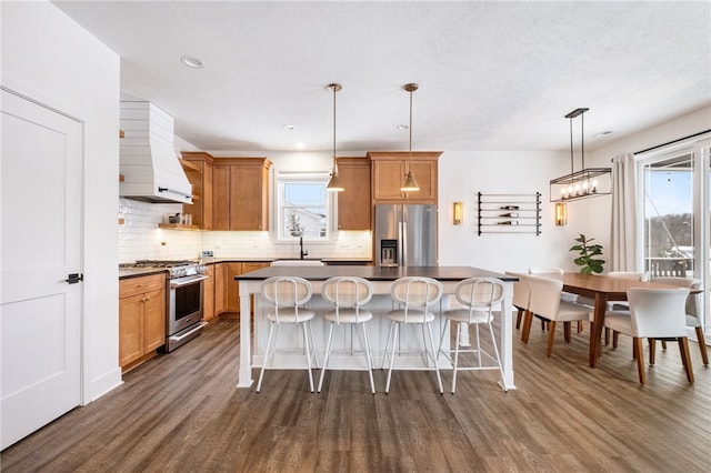 kitchen featuring custom range hood, stainless steel appliances, dark wood-type flooring, a kitchen island, and hanging light fixtures