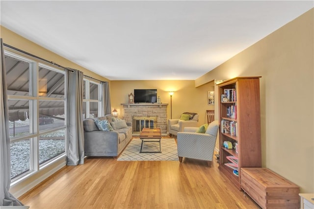 living room with a stone fireplace and light wood-type flooring