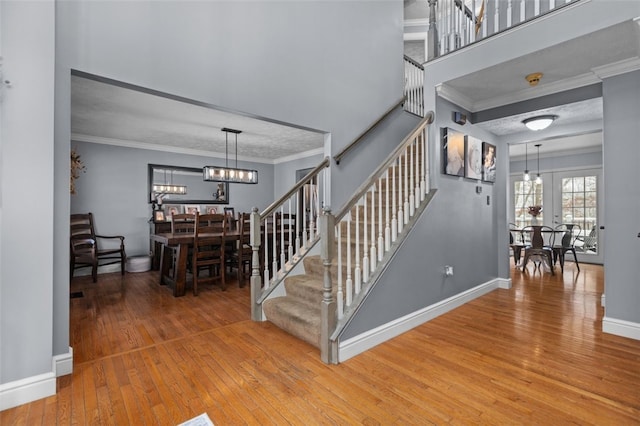 stairway with french doors, an inviting chandelier, crown molding, wood-type flooring, and a textured ceiling