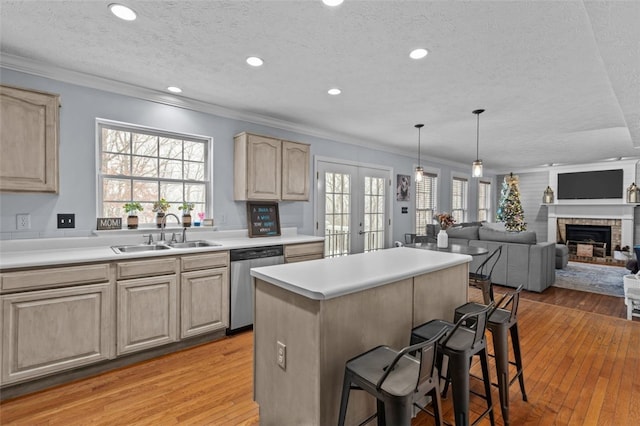 kitchen featuring sink, a brick fireplace, stainless steel dishwasher, light brown cabinetry, and a breakfast bar area