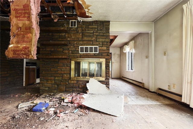 unfurnished living room featuring baseboard heating, a stone fireplace, and a textured ceiling